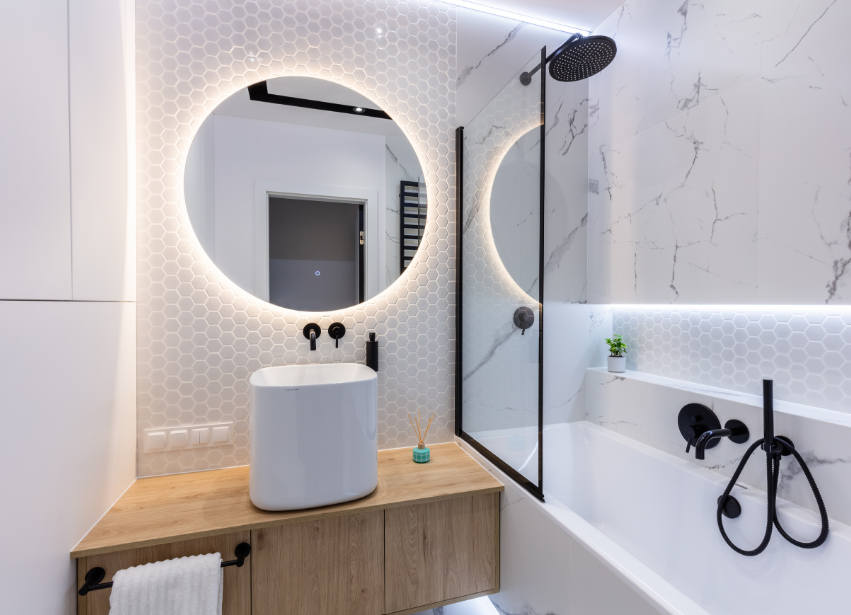 Compact bathroom with round lit mirror and bath shower combination
